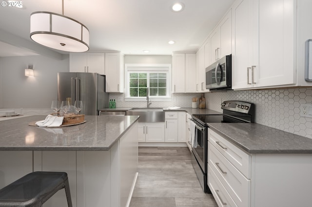 2823 SE Olsen St, Milwaukie, OR 97222 - kitchen with stainless steel appliances, a sink, light wood-style floors, white cabinetry, and dark stone countertops