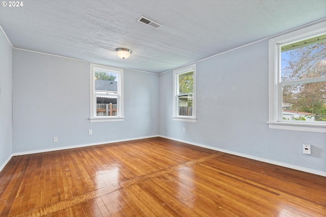 empty room featuring a textured ceiling, hardwood / wood-style flooring, and plenty of natural light