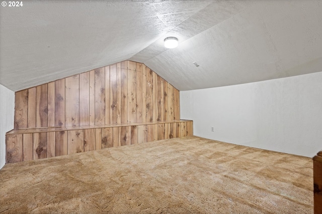 bonus room featuring carpet, vaulted ceiling, a textured ceiling, and wood walls