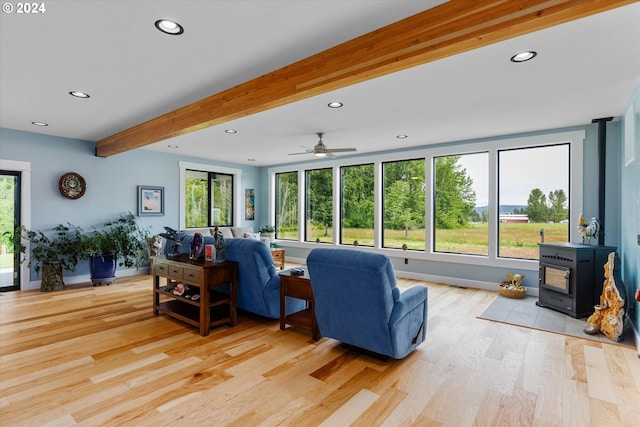 living room with ceiling fan, beam ceiling, a wood stove, and light hardwood / wood-style flooring