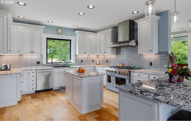 kitchen with white cabinetry, pendant lighting, stainless steel appliances, and wall chimney range hood