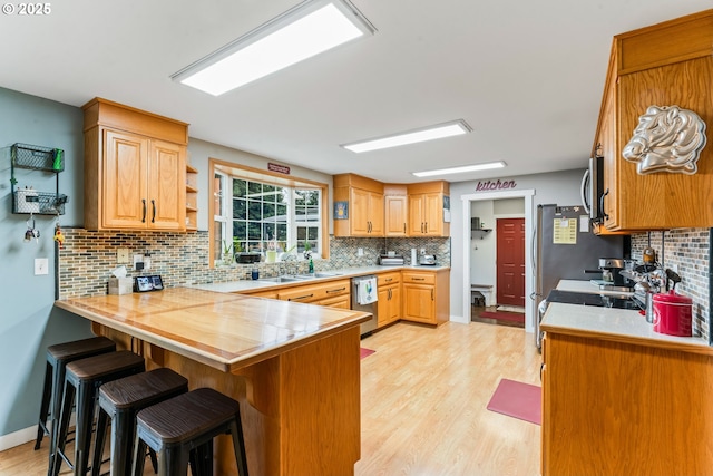 kitchen featuring stainless steel appliances, sink, kitchen peninsula, light wood-type flooring, and a breakfast bar