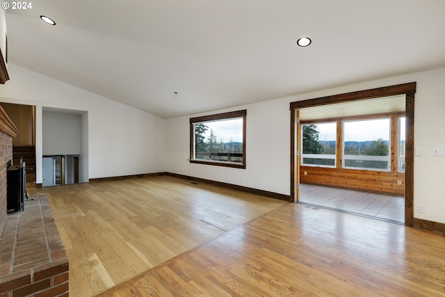 unfurnished living room featuring a brick fireplace, vaulted ceiling, and light hardwood / wood-style flooring