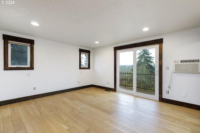 unfurnished room with an AC wall unit, a textured ceiling, and light wood-type flooring