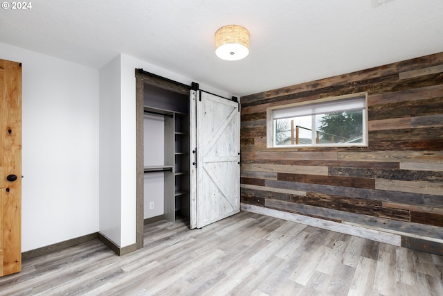 unfurnished bedroom with a barn door, light hardwood / wood-style floors, a closet, and wood walls