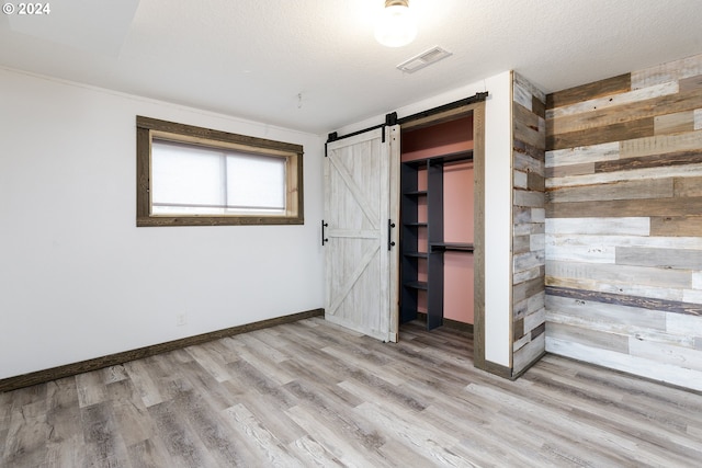 unfurnished bedroom featuring a barn door, light hardwood / wood-style flooring, a textured ceiling, wooden walls, and a closet