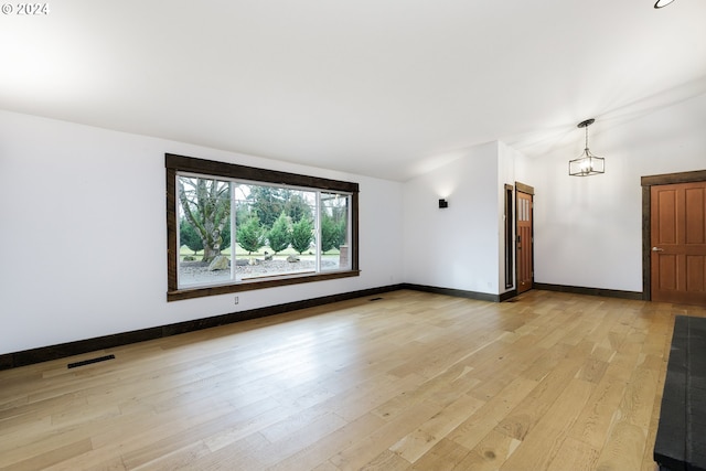 empty room featuring a notable chandelier and light wood-type flooring