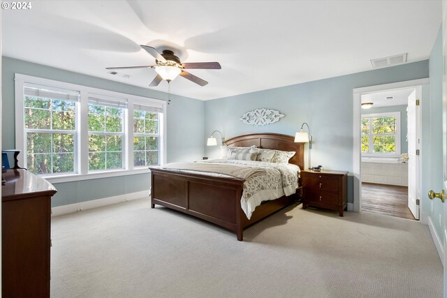 bedroom with ensuite bath, multiple windows, light colored carpet, and ceiling fan