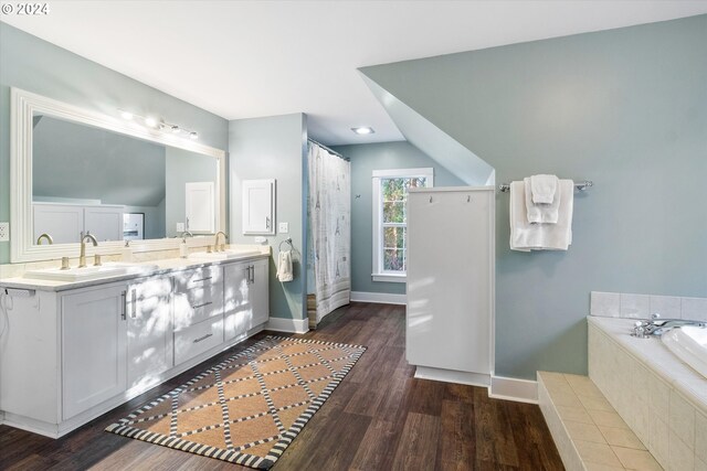 bathroom featuring vanity, hardwood / wood-style floors, tiled tub, and lofted ceiling