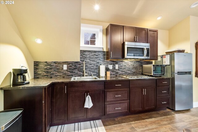 kitchen featuring decorative backsplash, wood-type flooring, dark stone counters, sink, and stainless steel appliances