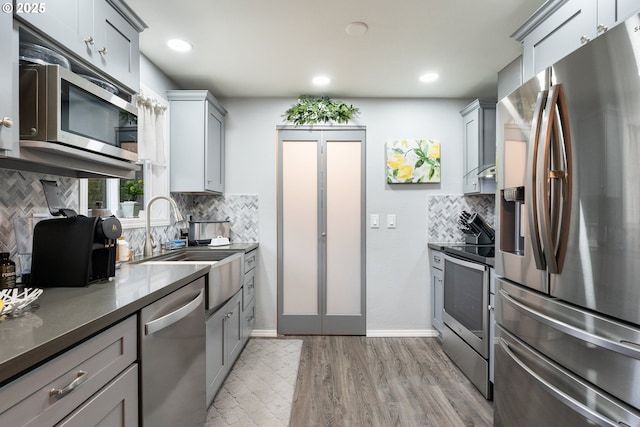 kitchen featuring sink, light hardwood / wood-style flooring, appliances with stainless steel finishes, gray cabinetry, and decorative backsplash