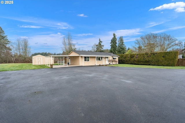 ranch-style home with a carport, a storage unit, and a front lawn