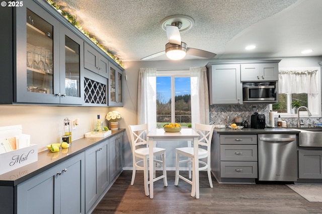 kitchen featuring gray cabinets, ceiling fan, appliances with stainless steel finishes, dark hardwood / wood-style floors, and tasteful backsplash