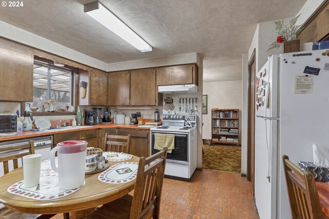 kitchen featuring a textured ceiling, backsplash, white appliances, and sink