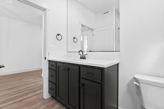 bathroom featuring visible vents, toilet, wood finished floors, baseboards, and vanity