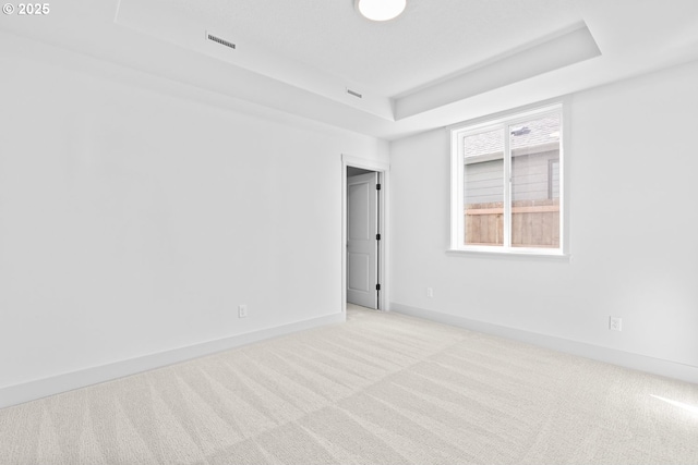 empty room featuring baseboards, a tray ceiling, light carpet, and visible vents