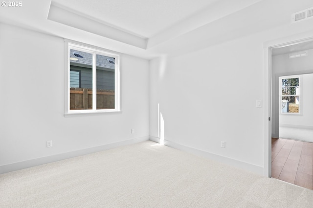 carpeted empty room with visible vents, baseboards, and a tray ceiling