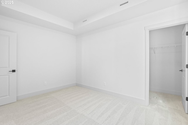 unfurnished bedroom with visible vents, a walk in closet, baseboards, light colored carpet, and a closet