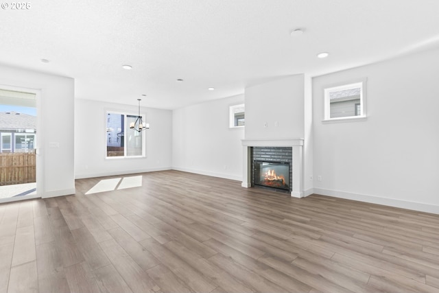 unfurnished living room with a notable chandelier, wood finished floors, a glass covered fireplace, recessed lighting, and baseboards