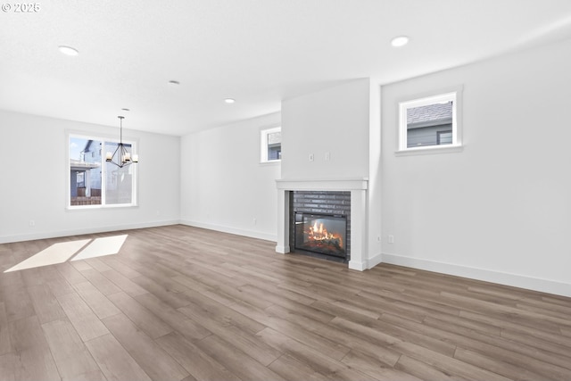 unfurnished living room featuring a glass covered fireplace, baseboards, an inviting chandelier, and wood finished floors