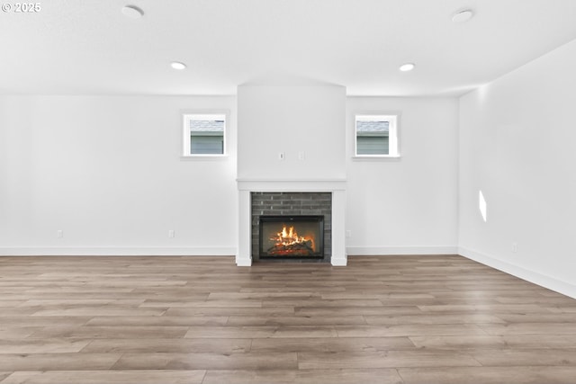 unfurnished living room with recessed lighting, a healthy amount of sunlight, light wood finished floors, and a lit fireplace