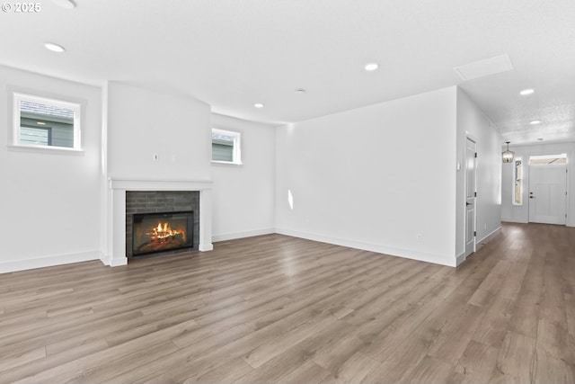 unfurnished living room with a glass covered fireplace, recessed lighting, light wood-type flooring, and baseboards