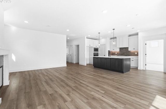 kitchen featuring backsplash, open floor plan, light wood-type flooring, a glass covered fireplace, and white cabinetry