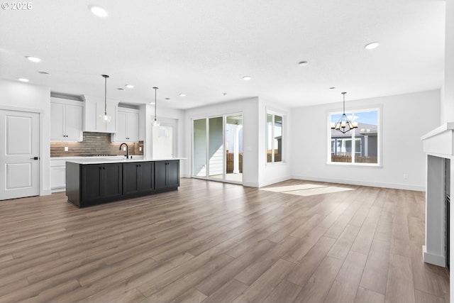 kitchen featuring light wood finished floors, an island with sink, light countertops, a notable chandelier, and tasteful backsplash