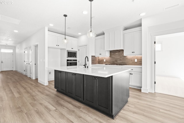 kitchen with stainless steel microwave, oven, stovetop, white cabinets, and a sink