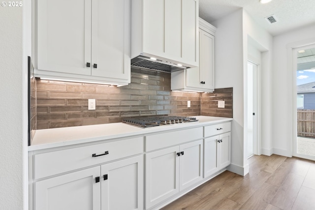 kitchen featuring visible vents, under cabinet range hood, decorative backsplash, stainless steel gas stovetop, and white cabinetry