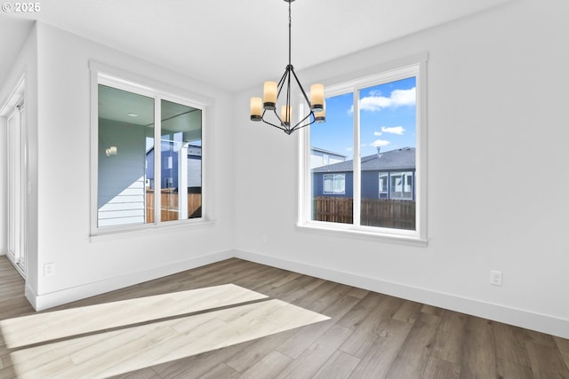 unfurnished dining area with an inviting chandelier, baseboards, and wood finished floors