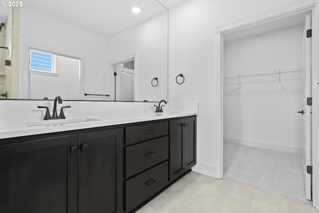 bathroom featuring a walk in closet, double vanity, tile patterned flooring, and a sink