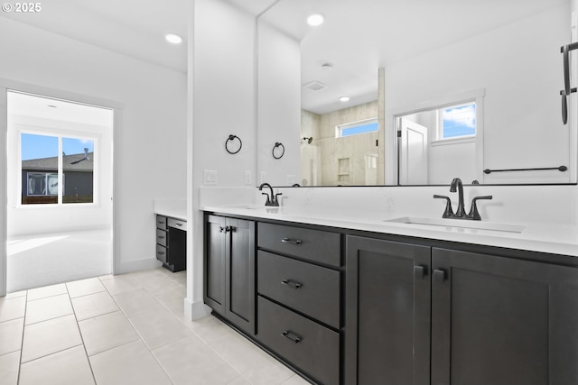 bathroom with double vanity, tile patterned flooring, tiled shower, and a sink