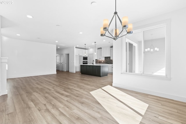 unfurnished living room with a chandelier, light wood-style flooring, and baseboards