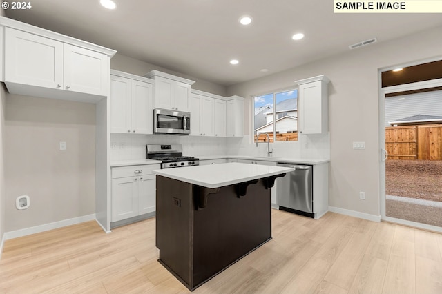 kitchen featuring sink, light wood-type flooring, appliances with stainless steel finishes, a kitchen island, and white cabinetry