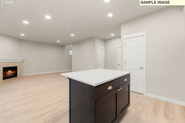 kitchen featuring dark brown cabinets, a kitchen island, a fireplace, and light hardwood / wood-style flooring