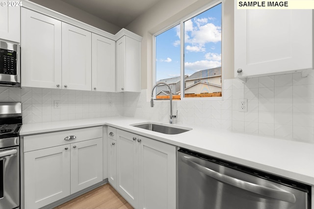 kitchen with sink, decorative backsplash, light wood-type flooring, white cabinetry, and stainless steel appliances