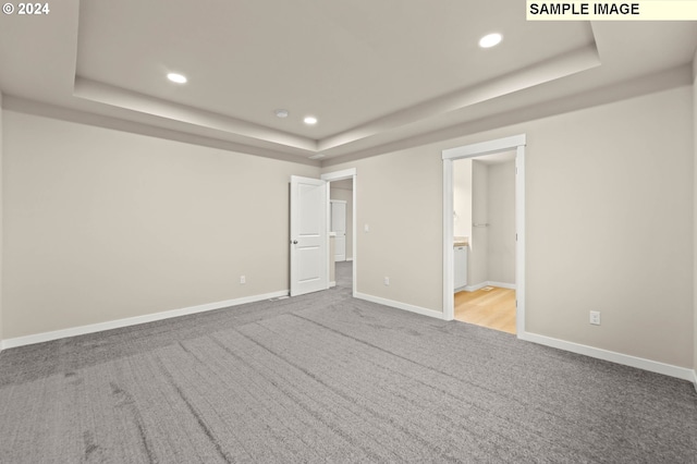 unfurnished bedroom featuring a tray ceiling, ensuite bathroom, and light colored carpet