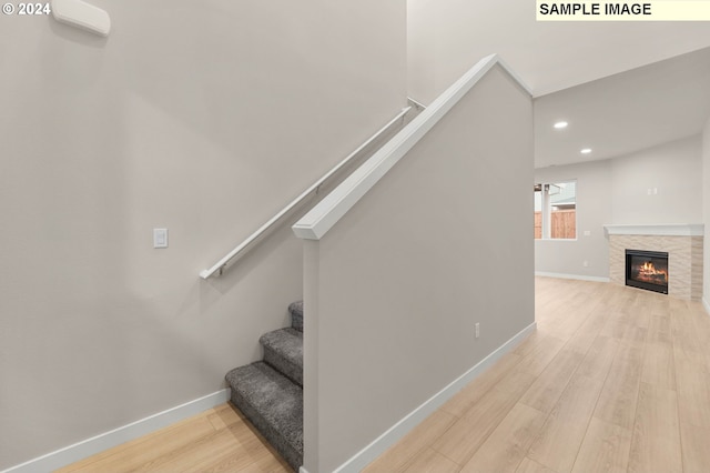 stairway with hardwood / wood-style flooring and a stone fireplace