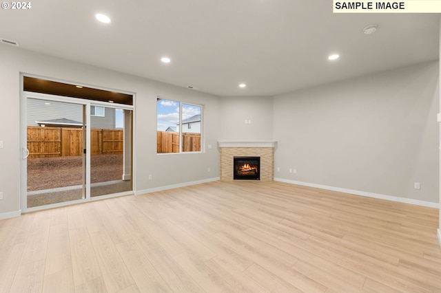 unfurnished living room featuring light hardwood / wood-style floors and a stone fireplace