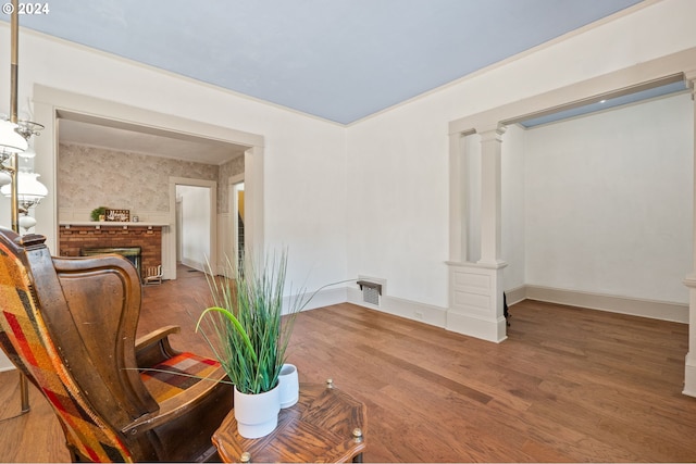 interior space featuring wood-type flooring, decorative columns, and a brick fireplace