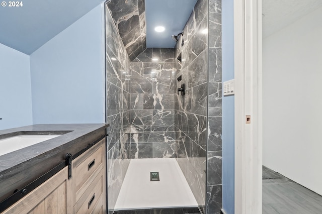 bathroom with tiled shower, vanity, and vaulted ceiling