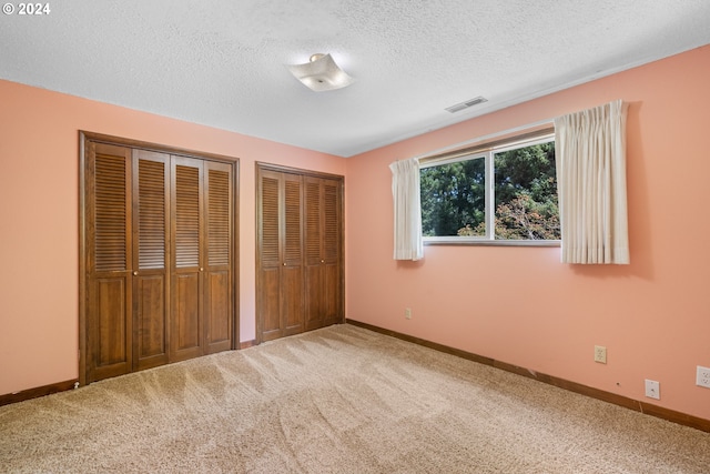 unfurnished bedroom with multiple closets, a textured ceiling, and carpet flooring