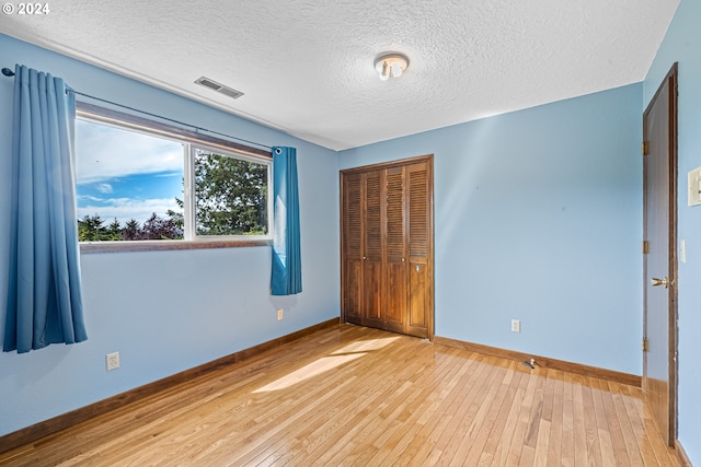 unfurnished bedroom featuring light wood-type flooring, a textured ceiling, and a closet