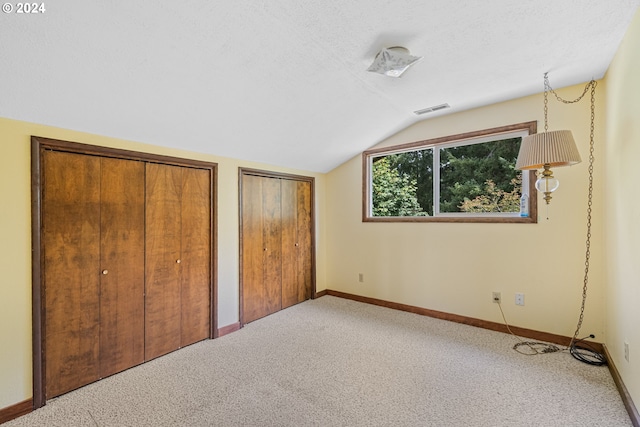 unfurnished bedroom with lofted ceiling, carpet flooring, multiple closets, and a textured ceiling