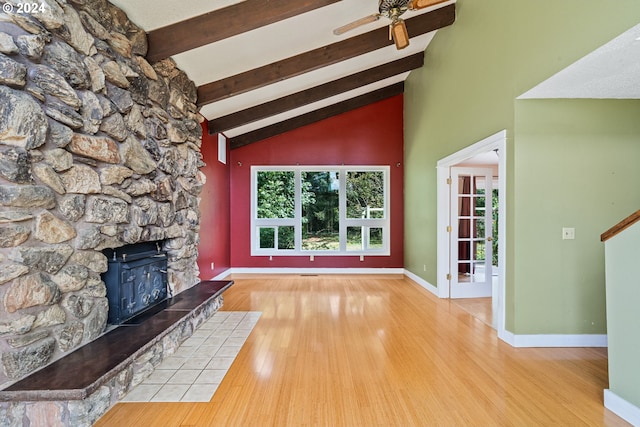 unfurnished living room featuring high vaulted ceiling, light hardwood / wood-style flooring, ceiling fan, a stone fireplace, and beam ceiling