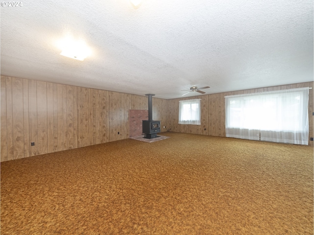 unfurnished living room featuring a textured ceiling, wooden walls, carpet, and a wood stove