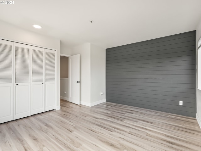 unfurnished bedroom featuring light hardwood / wood-style flooring, a closet, and wood walls