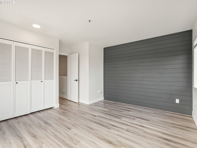 unfurnished bedroom with light hardwood / wood-style flooring, a closet, and wood walls