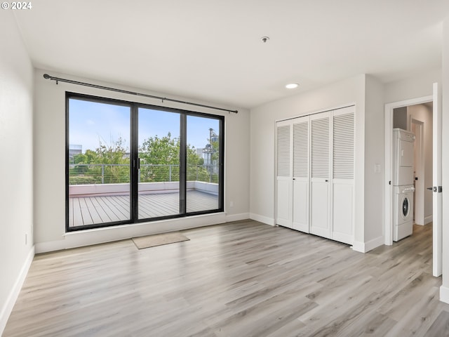 unfurnished bedroom featuring a closet, light hardwood / wood-style flooring, and stacked washing maching and dryer